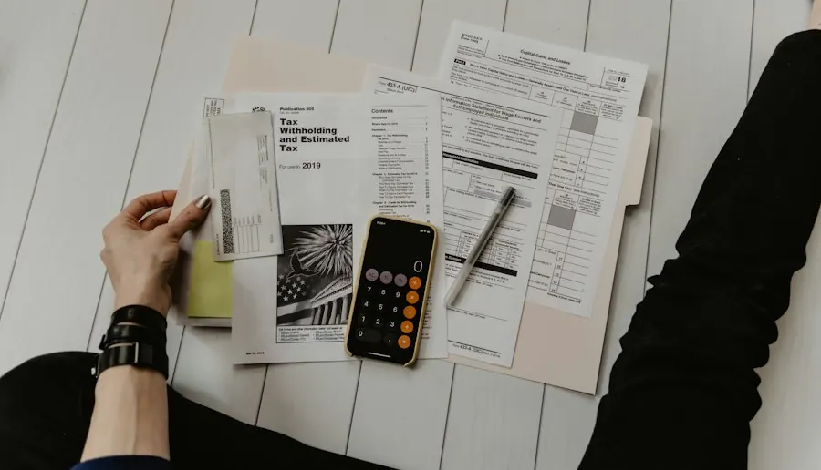 Bàn tay cầm chứng từ thuế, bên cạnh điện thoại bật máy tính và cây bút